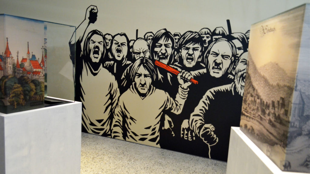 Ein Mob geht auf ein Opfer los: Wandbild in der «Sündenbock»-Ausstellung. | © Regula Pfeifer