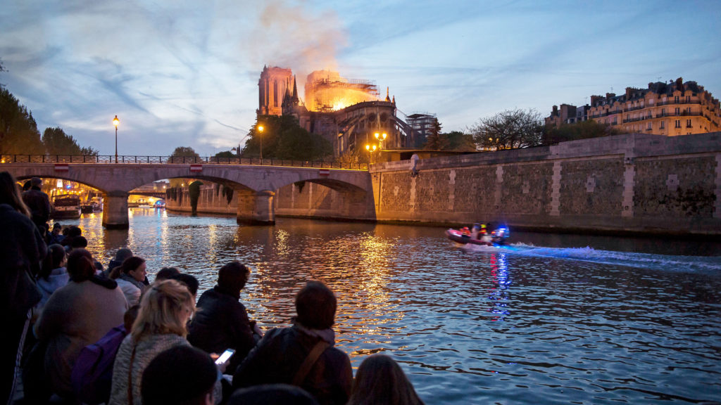 Menschen stehen am Ufer der Seine und blicken auf den Brand der Kathedrale Notre-Dame in Paris am 15. April 2019. | © KNA-Bild

