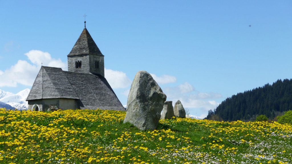 Die Steinsetzungen im bündnerischen Falera gelten als auf den Sonnenlauf, den Mond und die Sterne ausgerichtet. Im Hintergrund sieht man die Kirche St. Remigius. | © Wikimedia/Adrian Michael