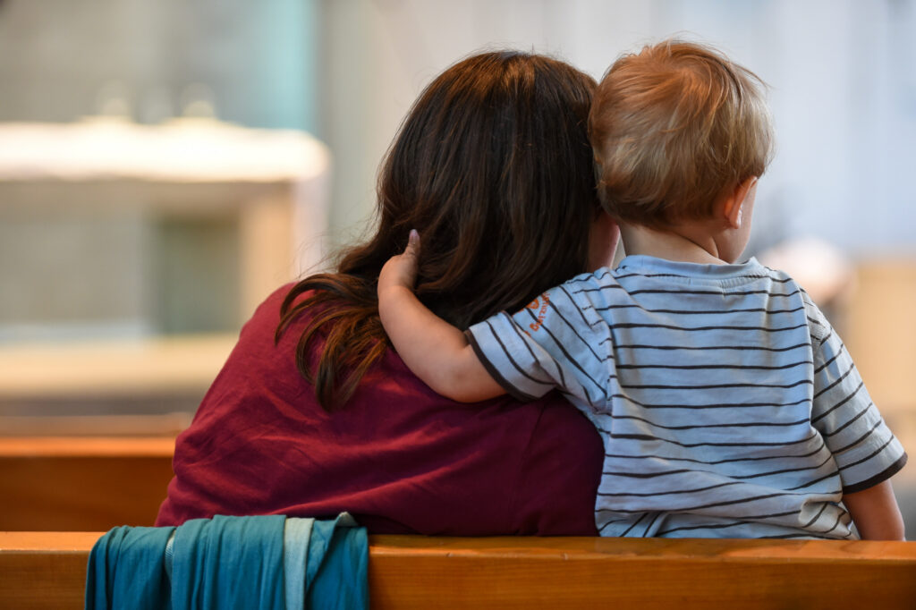 Eine Mutter sitzt mit ihrem Kind in einer Kirchenbank bei einem Familiengottesdienst. | © kna-bild.de