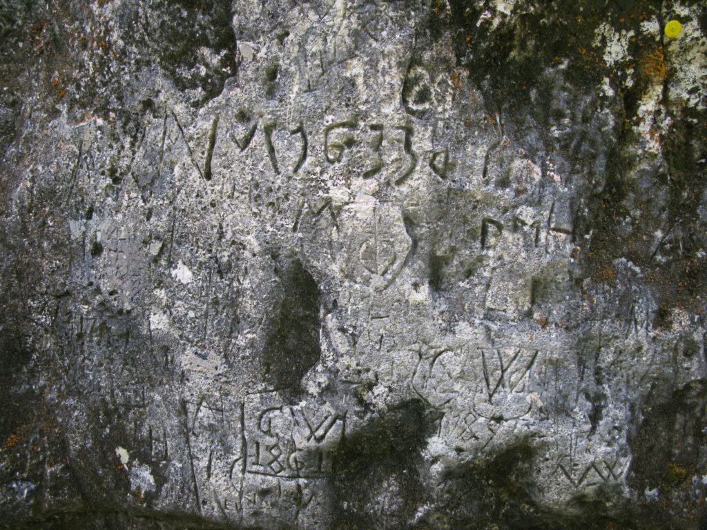 In der Felswand unter der eingestürzten Brücke sind zahlreiche Buchstaben, Zahlen und Zeichen aus unterschiedlichen Zeitabschnitten eingeritzt, die älteste erkennbare Jahrzahl ist 1633. | © Christian von Arx