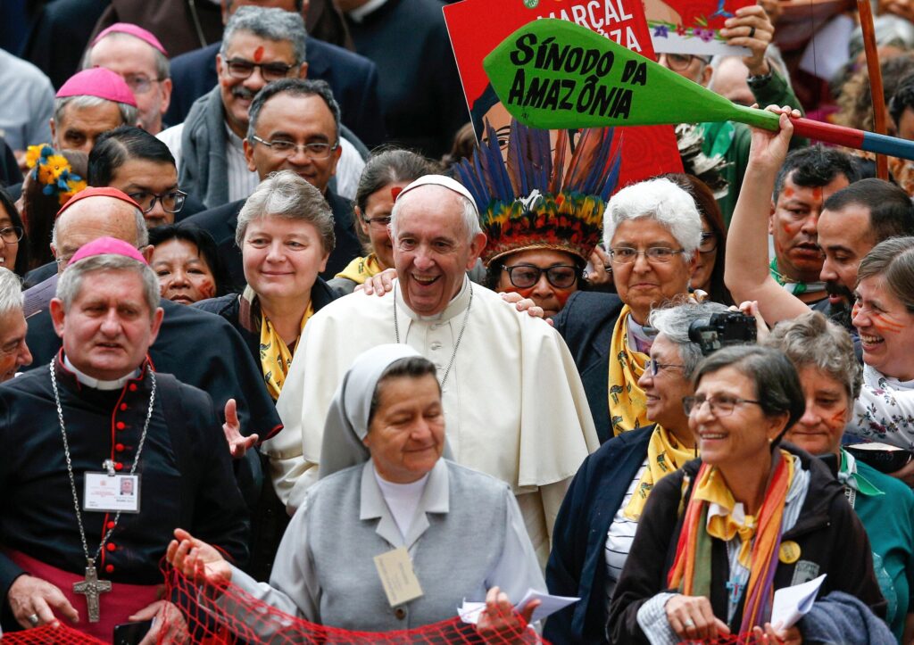 Lachend und umringt von Menschen: Zur Eröffnung der Amazonas-Bischofssynode am 7. Oktober 2019 im Vatikan zieht Papst Franziskus in einer Prozession mit Teilnehmerinnen und Teilnehmern in die Synodenaula ein. | © kna-bild.de