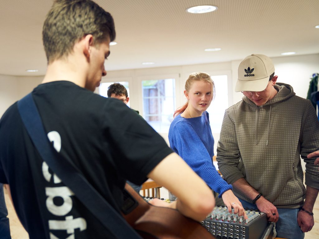 Drei junge Tontechniker/innen lösen während eines Kurses eine praktische Aufgabe im Bandraum des Kirchgemeindehauses.| © Gerry Amstutz